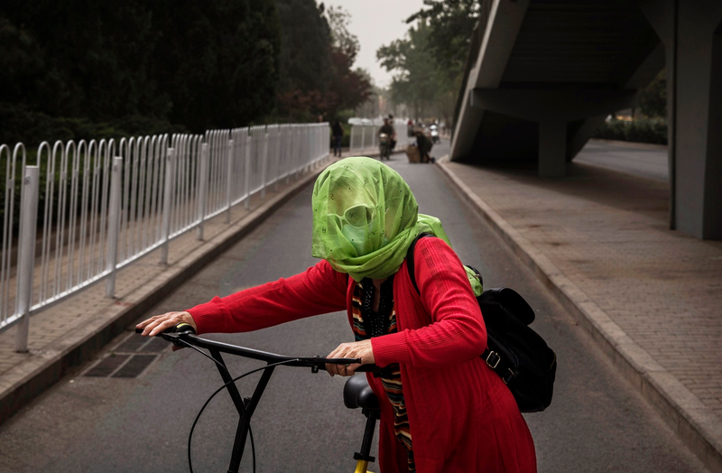 A Chinese woman wears a scarf around her head to protect from particles blown in during a sandstorm as she gets on her bike on May 4, 2017 in Beijing, China. (Photo by Kevin Frayer/Getty Images)